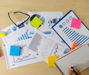 Desk with charts, graphs, sticky notes, and a person writing in a notebook, representing organized and secure research data handling