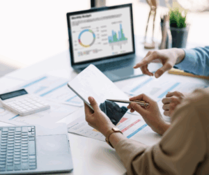 Team members reviewing data on a tablet and laptop surrounded by charts, graphs, and reports, representing Privileged Identity Management