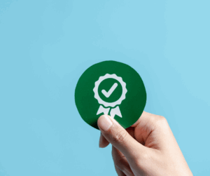 Hand holding a green circular badge with a check mark symbol, representing verified compliance and certification.